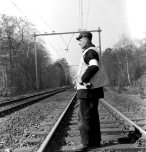 HUA-171737-Afbeelding van een veiligheidsman van de N.S. met signaalhoorn en geel vest op de spoorlijn ter hoogte van Driebergen-Zeist