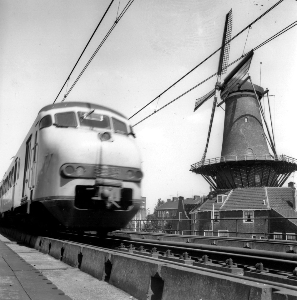 HUA-171791-Afbeelding van een electrisch treinstel mat. 1964 (plan V) van de N.S. op het spoorviaduct te Delft, met rechts de molen De Roos aan de Phoenixstraat