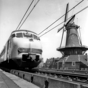 HUA-171791-Afbeelding van een electrisch treinstel mat. 1964 (plan V) van de N.S. op het spoorviaduct te Delft, met rechts de molen De Roos aan de Phoenixstraat