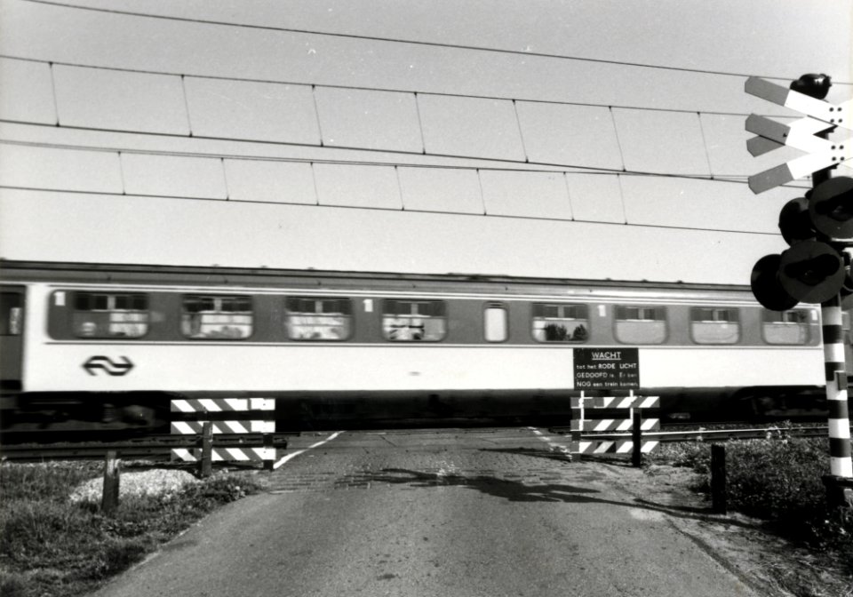 HUA-170277-Gezicht op een met een AKI (Automatische Knipperlicht Installatie) beveiligde spoorwegovergang, tijdens het passeren van een trein