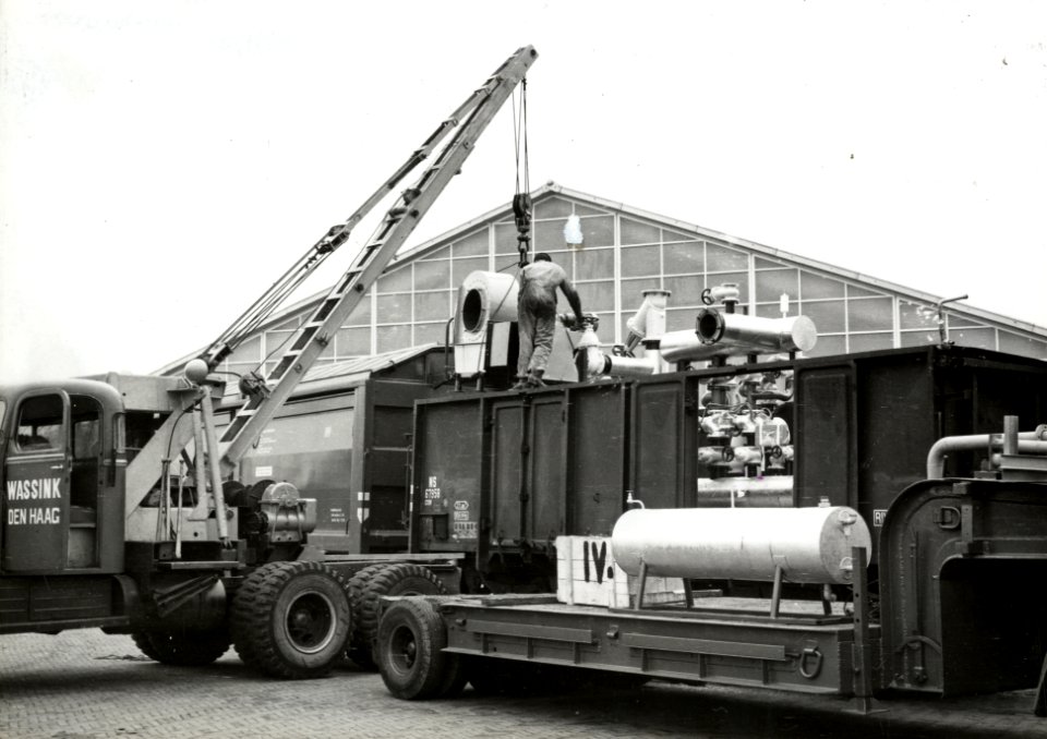 HUA-171246-Afbeelding van het vervoer van een oliestookinstallatie van de firma Boers en Vrijland (naar Roemenië) met een open goederenwagen (type GTOW) van de N.S. te 's-Gravenzande. Met behulp van een kraanwag