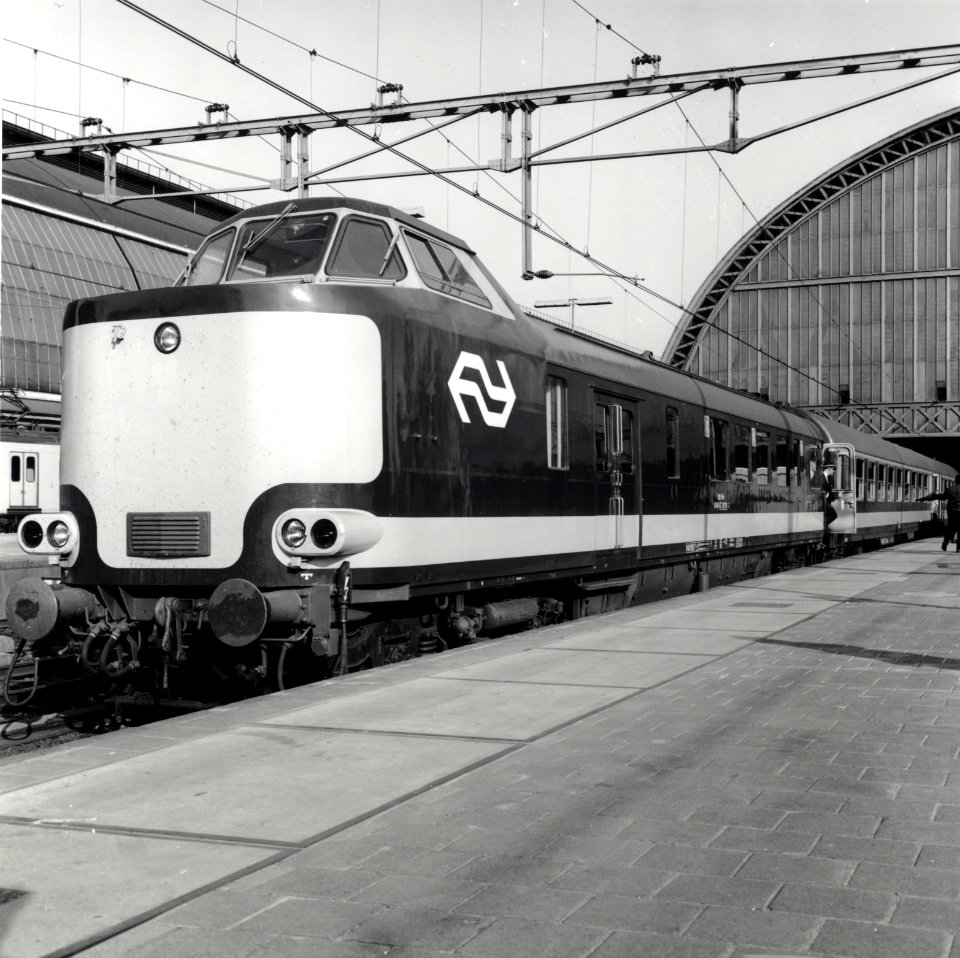 HUA-168173-Afbeelding van het stuurstandrijtuig 6184 87-38 101-3 van de N.S. (wRDk, ex-plan D) van een electrische Benelux trek-duweenheid van de N.S. en de N.M.B.S. langs het perron van het N.S.-station Amsterd