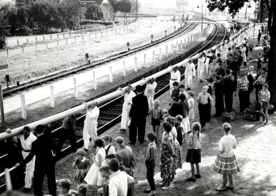 HUA-171254-Afbeelding van medewerkers van de firma Wavin te Hardenberg die onder grote publieke belangstelling drie 110 meter lange plastic buizen naar het station brengen voor transport naar Rotterdam
