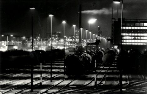HUA-170248-Gezicht op het emplacement te Pernis bij avond met rechts op de achtergrond het gebouw van SHELL