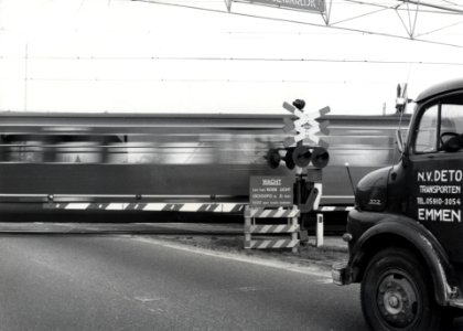 HUA-170532-Afbeelding van een AHOB bij een spoorwegovergang, tijdens het passeren van een trein, met rechts een gedeelte van een vrachtauto van de N.V. DETO te Emmen