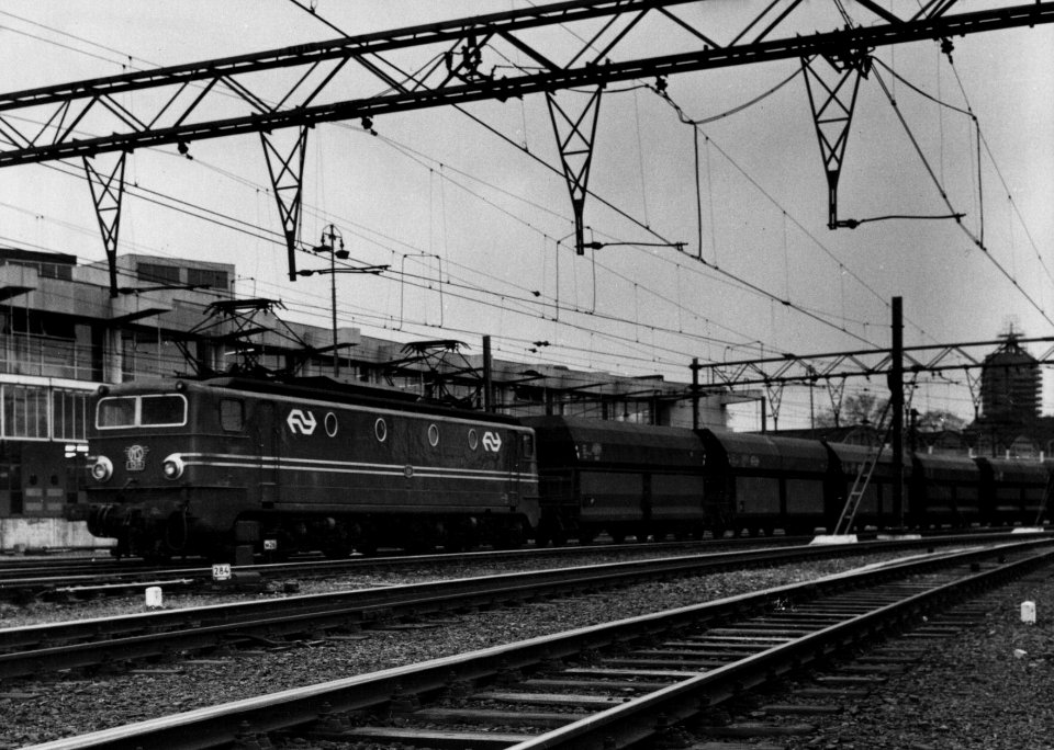 HUA-159888-Afbeelding van een goederentrein getrokken door een electrische locomotief uit de serie 1300 van de N.S. bij het N.S.-station Amsterdam C.S. te Amsterdam