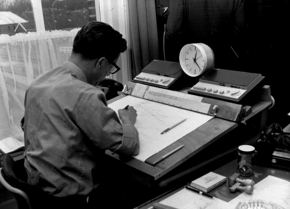 HUA-159734-Afbeelding van de treindienstleider in de CRVL-post (Centrale Radio Verkeersleiding) van de N.S. in het N.S.-station Usquert te Usquert, met blokbezettingsblad en mobilofooninstallatie. N.B. De CRVL w