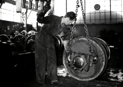 HUA-169939-Afbeelding van een werknemer van de hoofdwerkplaats van de N.S. te Tilburg tijdens het takelen van een wielstel in de wielendraaierij