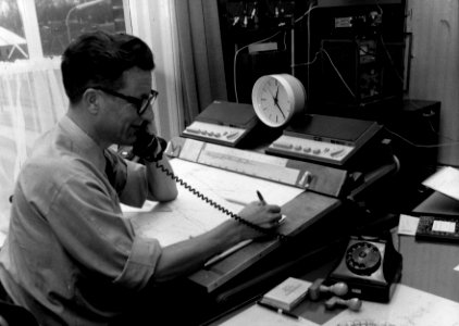 HUA-159737-Afbeelding van de treindienstleider in de CRVL-post (Centrale Radio Verkeersleiding) van de N.S. in het N.S.-station Usquert te Usquert, met blokbezettingsblad en mobilofooninstallatie. N.B. De CRVL w
