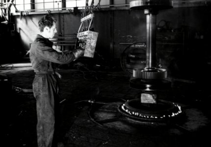 HUA-169936-Afbeelding van een werknemer van de hoofdwerkplaats van de N.S. te Tilburg tijdens het vervangen van een wielband in de wielendraaierij
