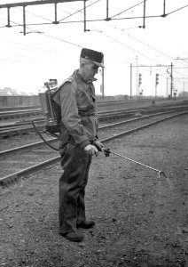 HUA-169054-Afbeelding van een wegwerker van de N.S. met een rugsproeier op het emplacement te 's-Hertogenbosch tijdens het bestrijden van onkruid