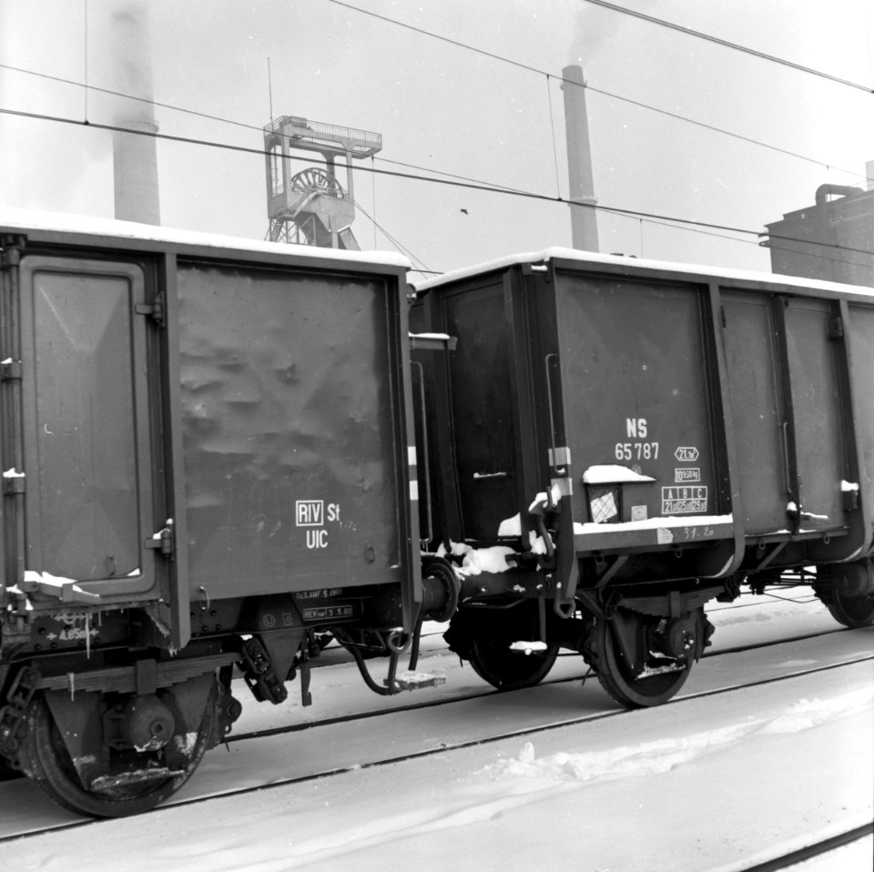 HUA-159807-Afbeelding van open goederenwagens voor het vervoer van steenkolen op het besneeuwde emplacement van de N.S. te Heerlen. Op de achtergrond de mijnschachttoren van de Oranje Nassau-mijn