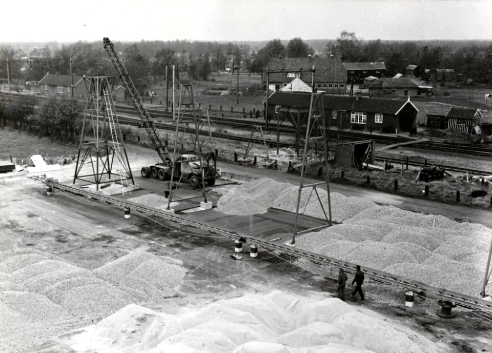 HUA-169084-Afbeelding van de aanleg van een tijdelijke bouwplaats voor het aannemersbedrijf Fa. P.C. Zanen N.V. ten behoeve van de aanleg van Rijksweg 1 langs de spoorlijn te Stroe. Op de achtergrond de dienstwo
