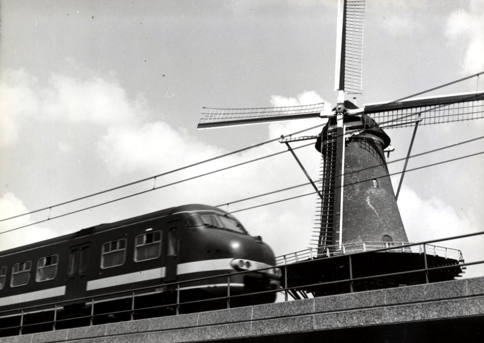HUA-169118-Gezicht op de molen De Roos aan de Phoenixstraat te Delft met op de voorgrond een electrisch treinstel plan V mat 1964 van de NS op het viaduct van he