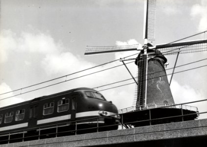 HUA-169118-Gezicht op de molen De Roos aan de Phoenixstraat te Delft met op de voorgrond een electrisch treinstel plan V mat 1964 van de NS op het viaduct van he