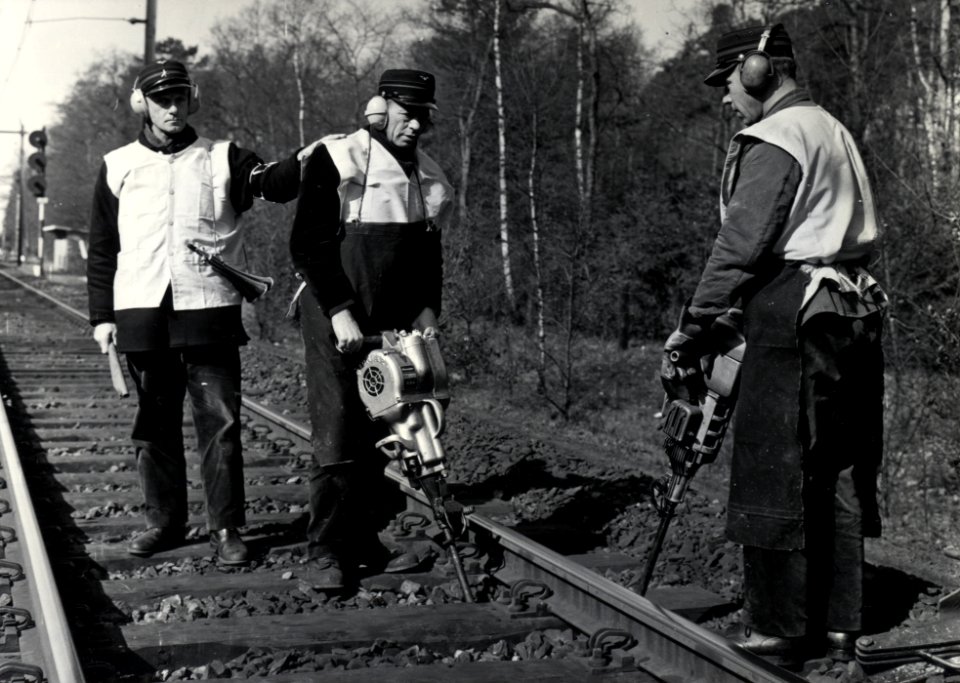 HUA-169036-Afbeelding van enkele wegwerkers van de N.S. met trilstanden tijdens onderhoudswerkzaamheden aan de spoorlijn nabij Driebergen-Zeist, met links een veiligheidsman