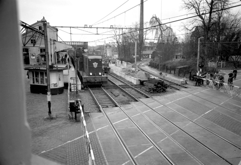 HUA-168892-Gezicht op de spoorwegovergang bij het N.S.-station Driebergen-Zeist te Driebergen-Rijsenburg, vanaf het seinhuis, tijdens de passage van een goederentrein getrokken door de diesel-electrische locomot
