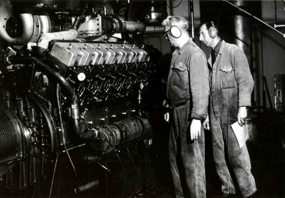 HUA-169915-Afbeelding van twee monteurs van de hoofdwerkplaats van de N.S. te Tilburg bij een dieselmotor, vermoedelijk in de proefstand voor dieselmotoren