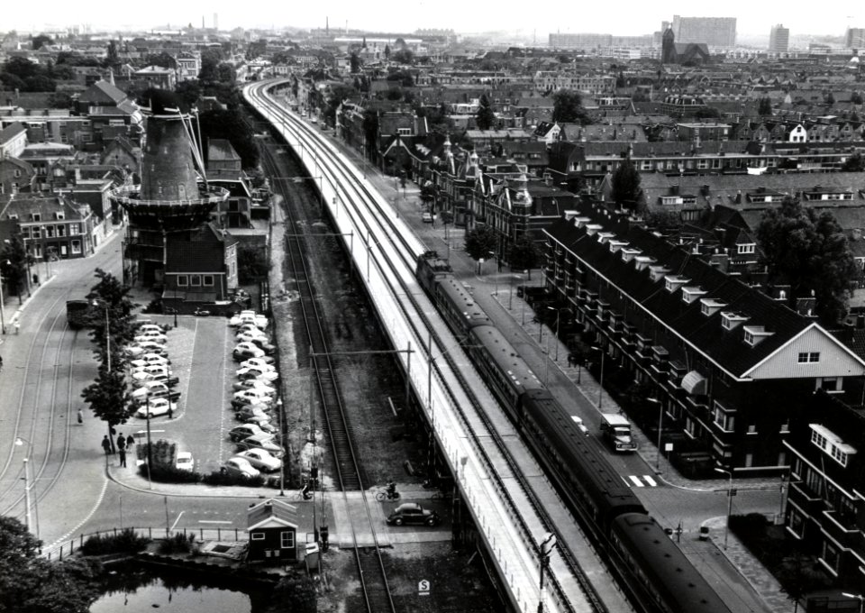 HUA-169114-Overzicht van de spoorlijn door Delft, vanaf het Bacinol-gebouw van de Gist- en Spiritusfabriek aan de Wateringsevest, met het oude, lage spoortracé waarvan nog één spoor resteert en rechts daarvan he