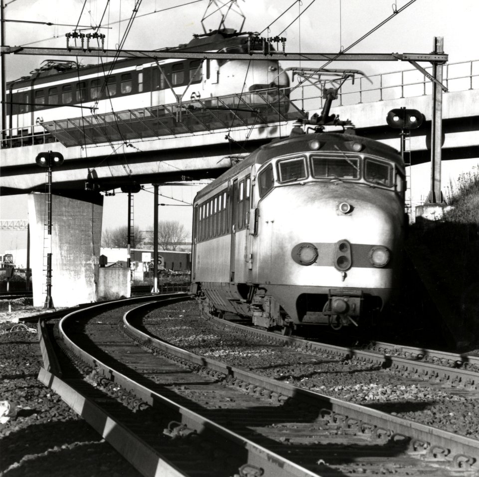 HUA-169169-Afbeelding van twee elkaar kruisende electirsche treinstellen mat. 1954 van de N.S. bij de fly-over aan de noordzijde van het emplacement van het N.S.-station Utrecht C.S. te Utrecht
