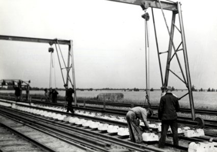 HUA-168928-Afbeelding van het monteren van spoorstaven op betonnen dwarsliggers ten behoeve van de spoorlijn tussen Helmond en Venlo