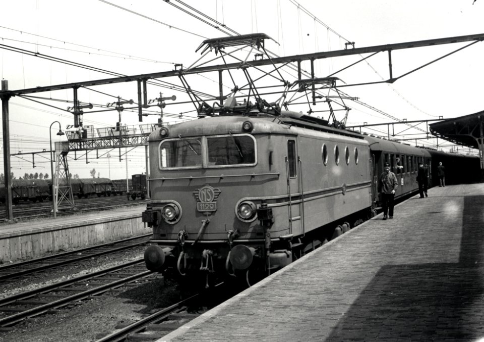 HUA-167993-Afbeelding van de electrische locomotief nr. 1129 (serie 1100) van de N.S. met een trein langs het perron van het N.S.-station Roosendaal te Roosendaal