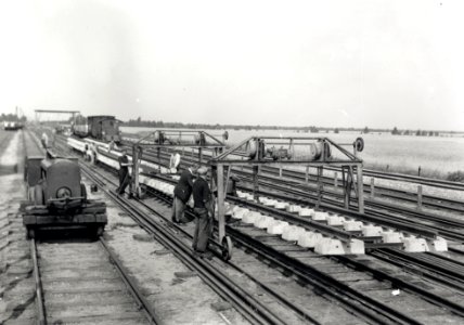 HUA-167971-Afbeelding van het verplaatsen van stukken spoor met betonnen dwarsliggers door middel van verrijdbare portaalkranen door wegwerkers van de NS op het 