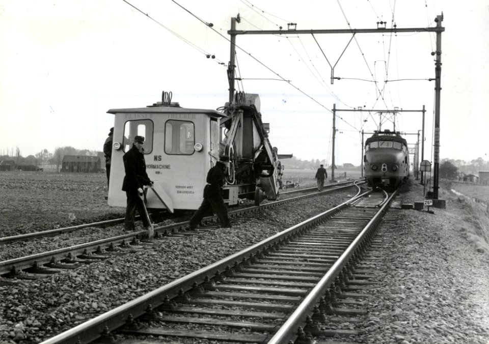 HUA-169660-Afbeelding van de hormachine van de N.S. tijdens onderhoudswerkzaamheden aan de spoorlijn te Heerhugowaard, met rechts een electrisch treinstel mat. 1954 (plan F)