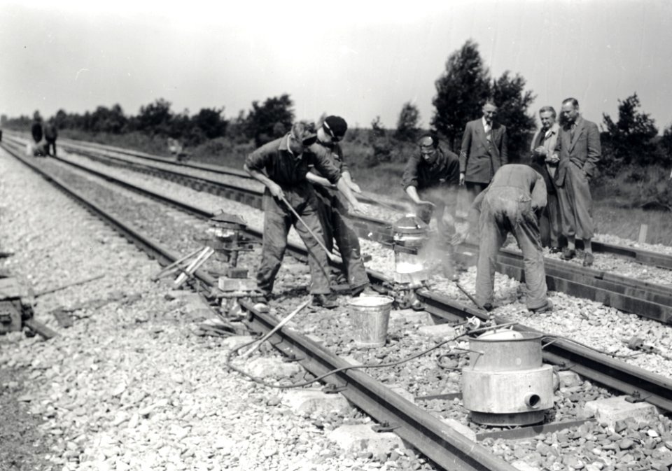 HUA-167977-Afbeelding van het aaneenlassen van stukken spoor met betonnen dwarsliggers door wegwerkers van de NS in de spoorlijn nabij Deurne