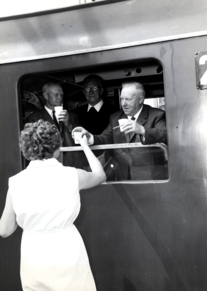 HUA-168829-Afbeelding van het uitdelen van koffie aan een groep bejaarden in de extra trein, bestaande uit rijtuigen plan D van de N.S., voor de reis van "Ouden van Dagen" op het N.S.-station Naarden-Bussum te B
