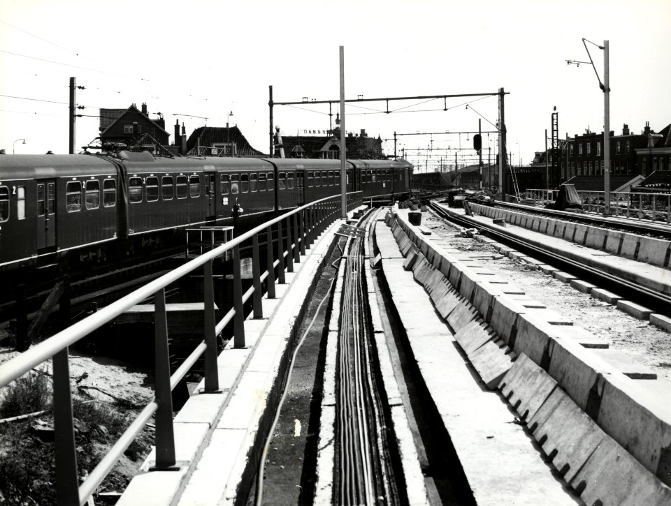 HUA-168611-Gezicht op het viaduct van het in aanleg zijnde hoogspoor door Delft, ter hoogte van het Bolwerk, met links een electrisch treinstel mat. 1940 van de N.S. op het lage (hulp-)tracé. Rechts op de achter