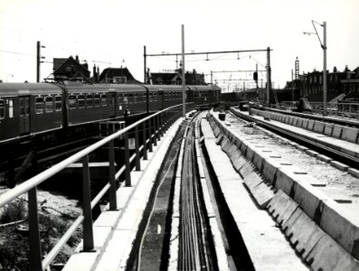 HUA-168611-Gezicht op het viaduct van het in aanleg zijnde hoogspoor door Delft, ter hoogte van het Bolwerk, met links een electrisch treinstel mat. 1940 van de N.S. op het lage (hulp-)tracé. Rechts op de achter