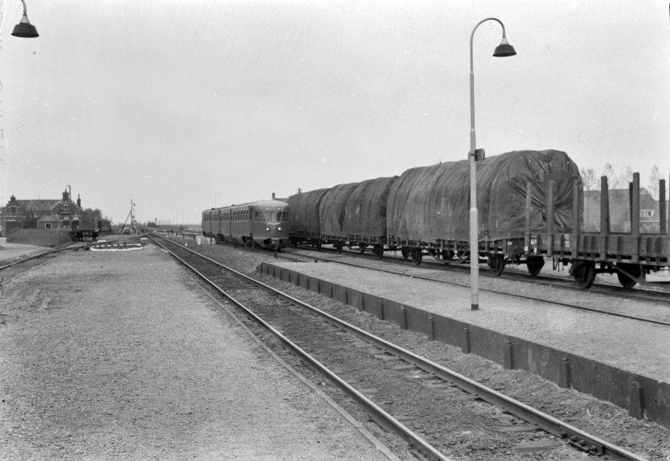 HUA-167500-Gezicht op het emplacement van het N.S.-station Baflo te Baflo, met enkele goederenwagens en een naderend diesel-electrisch treinstel DE 2 ("Blauwe Engel", serie 61-106) van de N.S