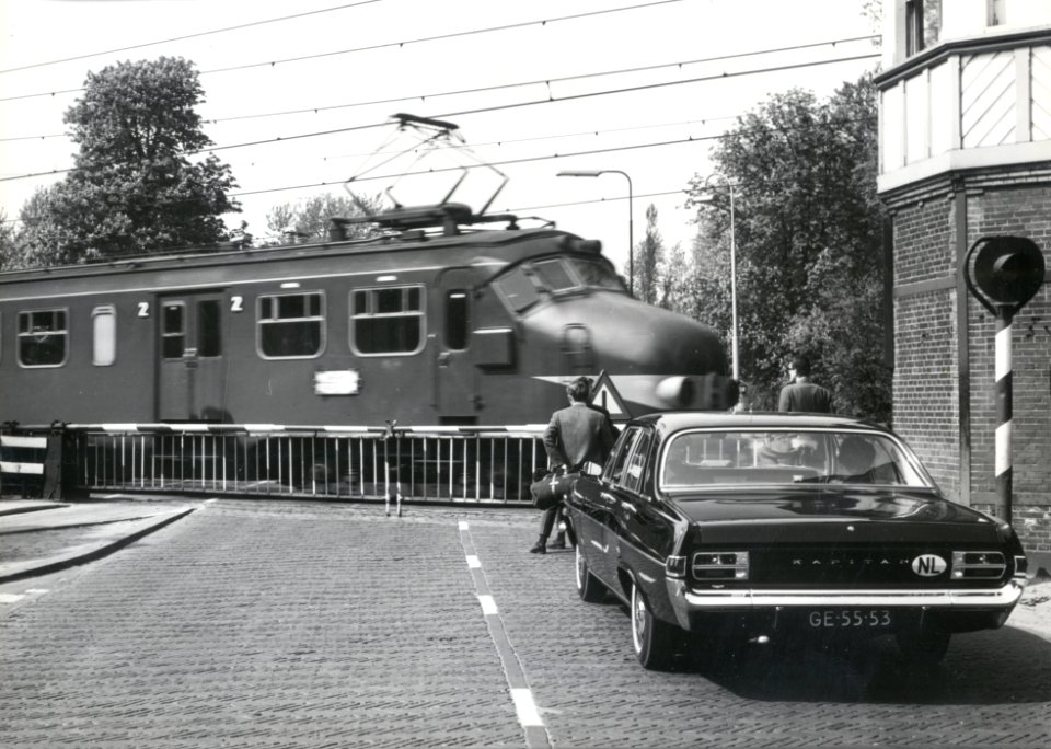 HUA-169396-Gezicht op de spoorwegovergang in de Hoofdstraat bij het NS station Driebergen Zeist te Driebergen Rijsenburg met gesloten overwegbomen en een passere