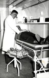 HUA-168747-Afbeelding van dr. J. Zwarteveen, chef van de medische afdeling van de N.S., die het zuurstofmasker demonstreert in de tot ambulance omgebouwde Crossley autobus van de N.S