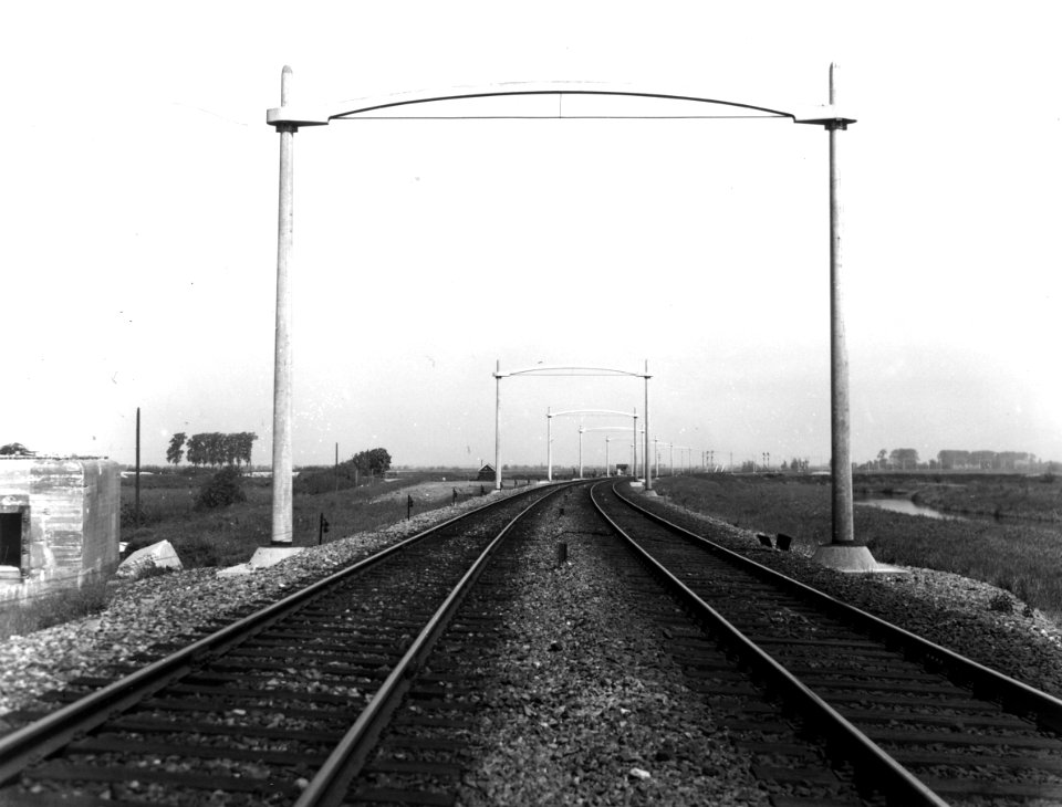 HUA-166402-Gezicht op de spoorlijn tussen Dordrecht en Lage Zwaluwe, ter hoogte van Moerdijk, met juist geplaatste betonnen bovenleidingsportalen ten behoeve van de electrificatie van de lijn
