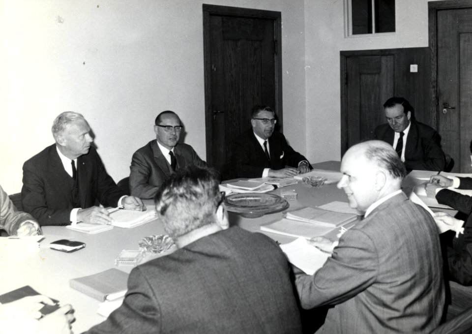 HUA-169344-Groepsportret van de concernleiding van de N.S. tijdens een vergadering, met van links naar rechts mr. W.J. de Graaff, mr. P.R. Leopold, mr. L.W. Wansink en ir. H. Zeydner. Op de voorgrond (op de rug 