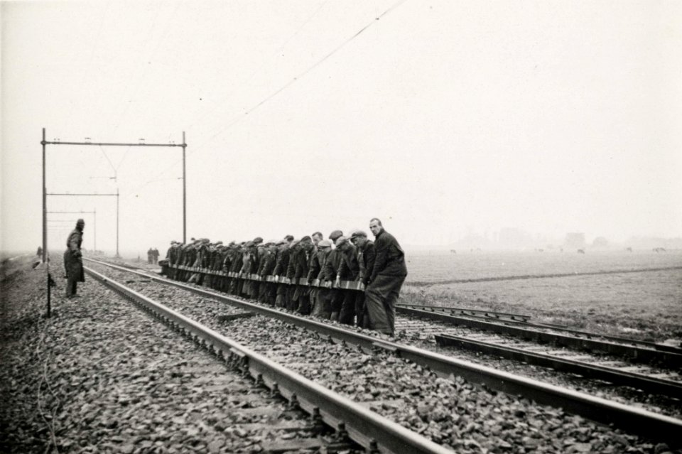 HUA-165753-Afbeelding van de werkzaamheden ten behoeve van de baanverzwaring tussen Amsterdam en Utrecht, ter hoogte van Duivendrecht, met een ploeg wegwerkers die een spoorstaaf verplaatsen