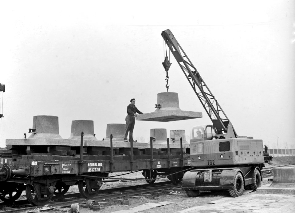HUA-166423-Afbeelding van het beladen van een rongenwagen met betonnen voeten voor bovenleidingsmasten puddingen te Lage Zwaluwe ten behoeve van de electrificati
