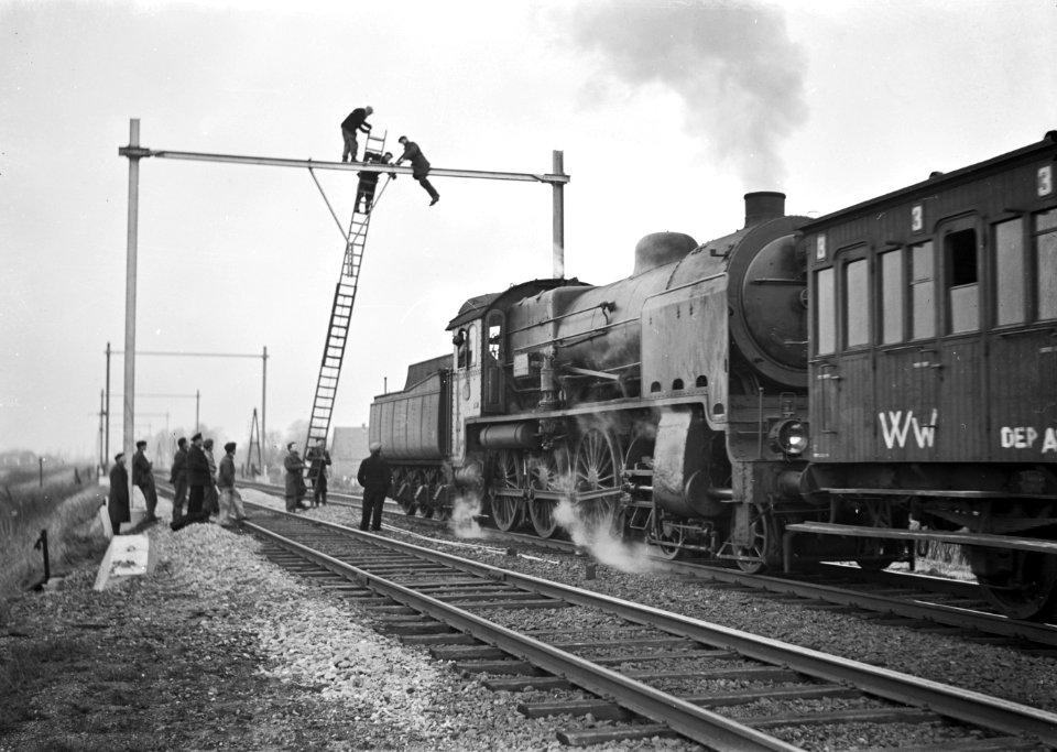 HUA-166451-Afbeelding van de montage van een bovenleidingsportaal op de spoorlijn tussen Dieren en Brummen, in verband met de electrificatie van het baanvak, met op de voorgrond een werktrein met een stoomlocomo