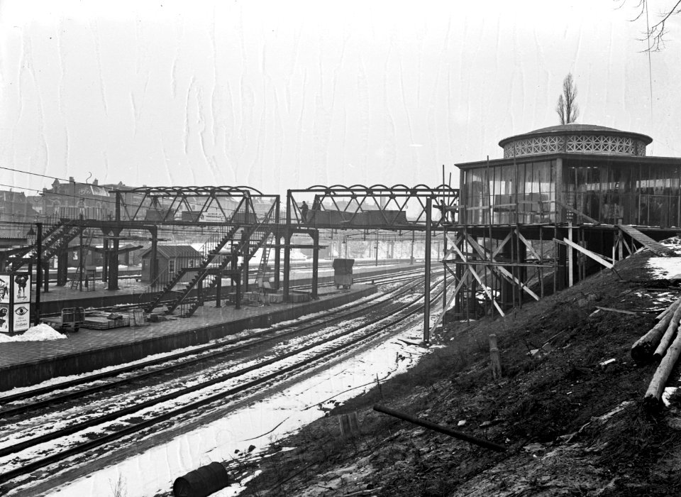 HUA-166233-Gezicht op de in aanbouw zijnde voetgangersbrug van het nieuwe N.S.-station Arnhem te Arnhem, met rechts de koepel van de ingang aan de Sonsbeekzijde van het station