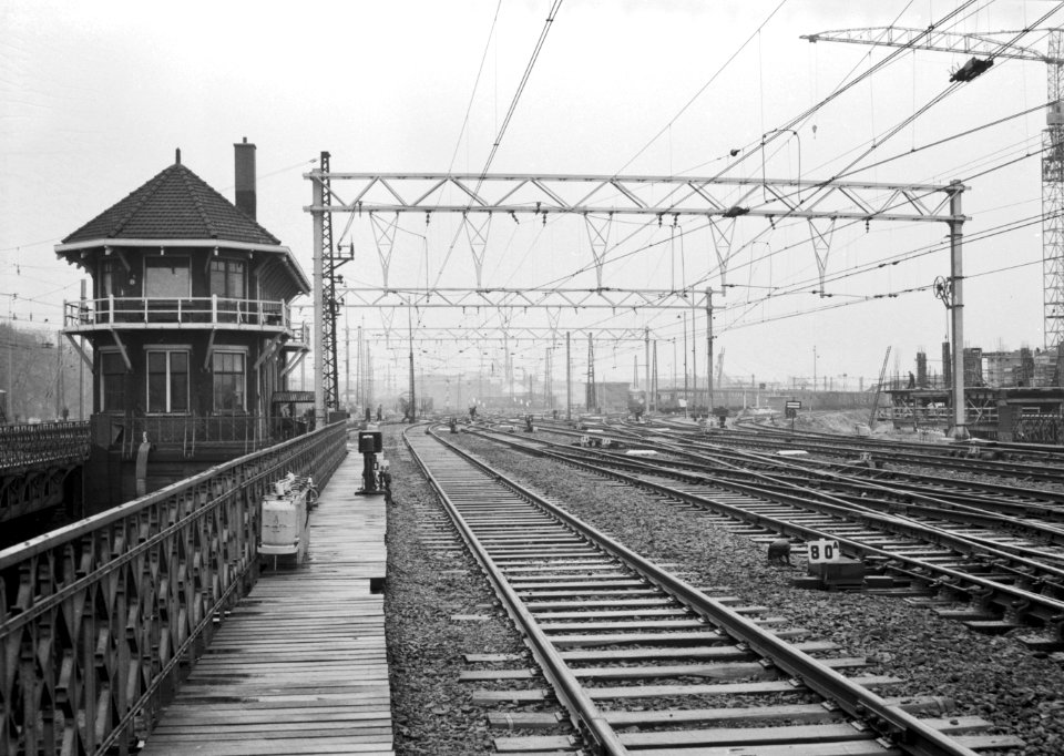 HUA-166439-Gezicht op het emplacement Westelijk Eiland bij het N.S.-station Amsterdam C.S., met bovenleidingsportalen voorzien van kokerbalkliggers. Links het seinhuis
