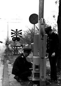 HUA-153324-Afbeelding van twee spoorwegpolitiebeambten bij een met een camera bewaakte spoorwegovergang