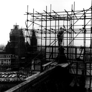 HUA-153773-Gezicht op het koperen beeld "Schilddrager van den Koning" op het dak van het Koninklijk paviljoen van het N.S.-station Amsterdam C.S. te Amsterdam met op de achtergrond de Nicolaaskerk