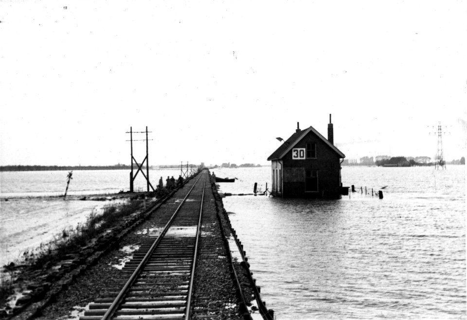 HUA-152845-Afbeelding van de herstelde spoorbaan door de Kruiningerpolder ("Badkuipspoorlijn") temidden van overstroomde landerijen bij wachtpost 30 (diensdoend als seinpost, zie de vlag uit het dakraam). nabij 