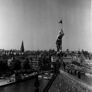 HUA-153772-Gezicht op het koperen beeld "Schilddrager van den Koning" op het dak van het Koninklijk paviljoen van het N.S.-station Amsterdam C.S. te Amsterdam met op de achtergrond de stad Amsterdam