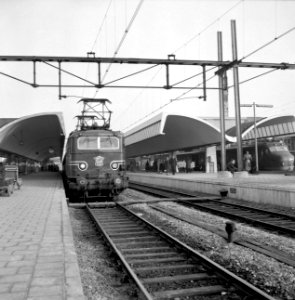 HUA-153214-Afbeelding van de electrische locomotief nr. 1125 (serie 1100) van de N.S. langs een perron van het N.S.-station Rotterdam C.S. te Rotterdam. Rechts staat een electrisch treinstel mat. 1954 van de N.S
