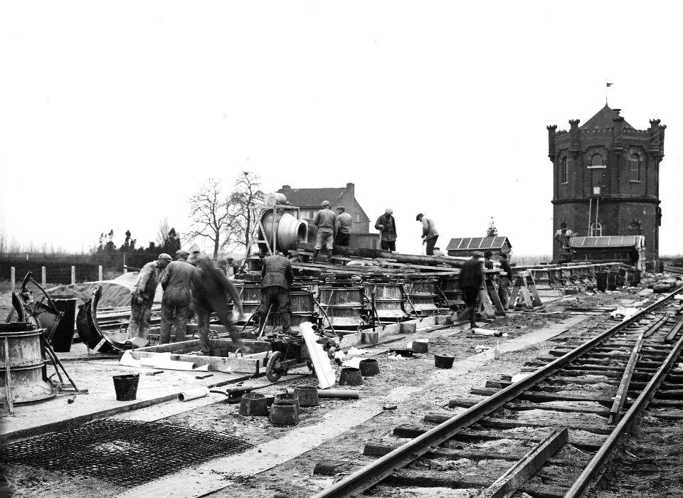 HUA-163805-Afbeelding van de fabricage van betonnen funderingsblokken ("puddingen") voor bovenleidingsmasten op het emplacement van het N.S.-station Lage Zwaluwe. Rechts op de achtergrond de oude watertoren