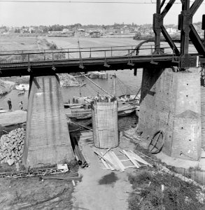 HUA-153621-Gezicht op de bouw van een pijler voor de nieuwe spoorbrug over de Maas bij Venlo met op de voorgrond de oude noodbrug