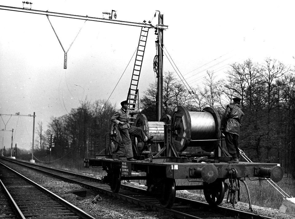 HUA-164029-Afbeelding van twee monteurs op een haspelwagen van de N.S. tijdens het "draadtrekken" voor de bovenleiding op de spoorlijn tussen Dieren en Brummen, ten behoeve van de electrificatie van de lijn Arnh